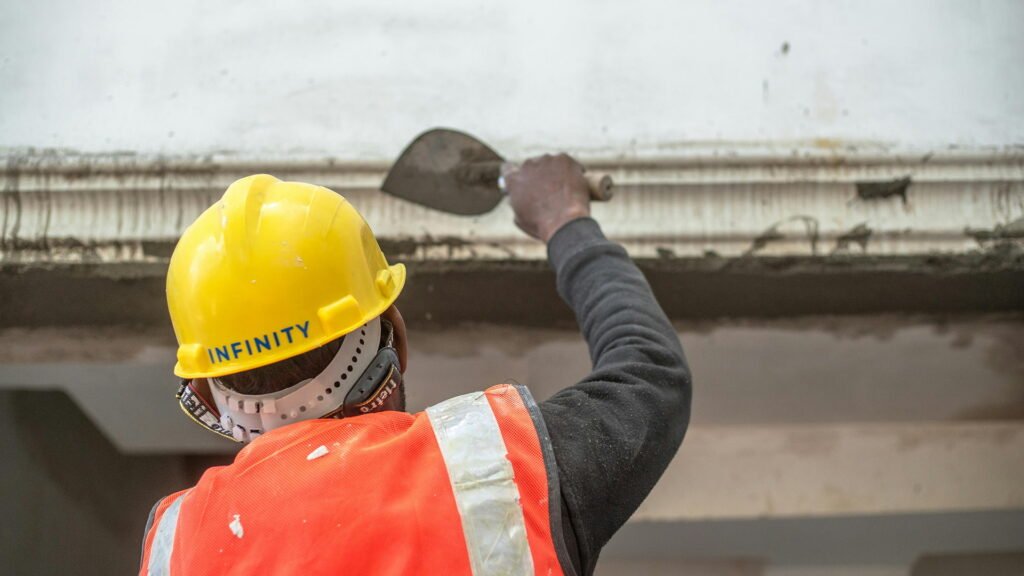 Construction worker applying plaster to a false ceiling edge while wearing a safety helmet and reflective vest during interior renovation work.