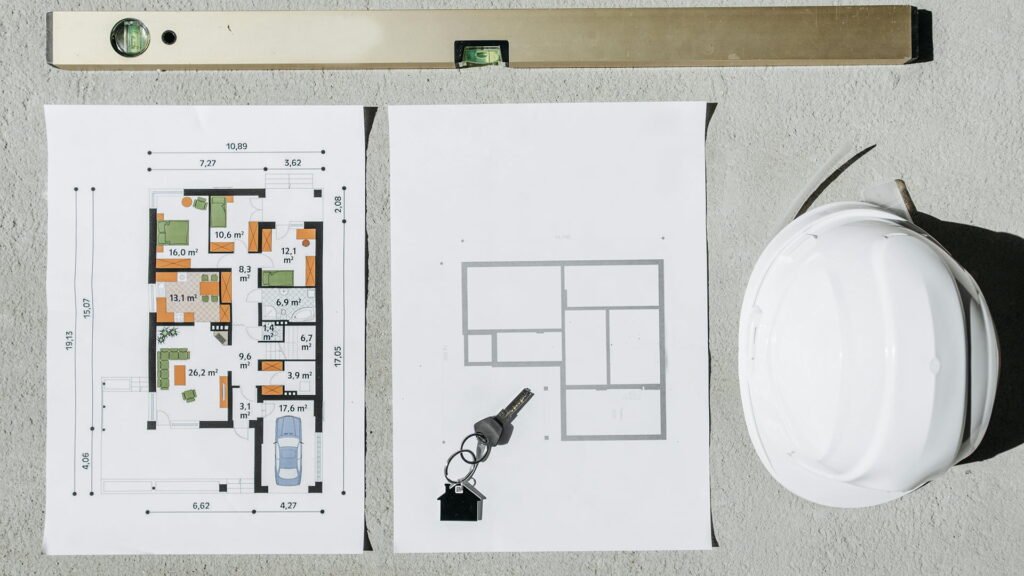 A detailed architectural workspace featuring colored house floor plans, a spirit level, keys with a home-shaped keychain, and a white safety helmet — symbolizing precision, planning, and modern construction design.